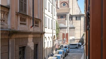 Une rue étroite bordée de bâtiments historiques, de voitures garées et d’un ciel d’un bleu éclatant.