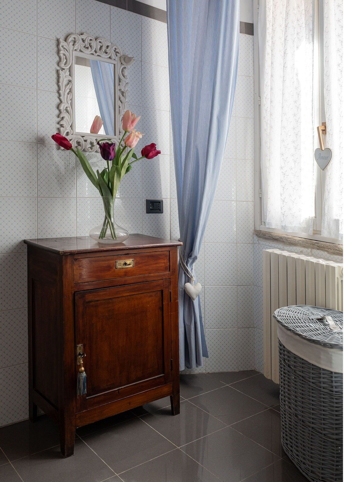 Ein Badezimmer mit Holzwaschtisch, einem Spiegel mit aufwendiger Rahmenfassung, einer Blumenvase, einem blauen, gestreiften Duschvorhang und einem Korbwäscher.