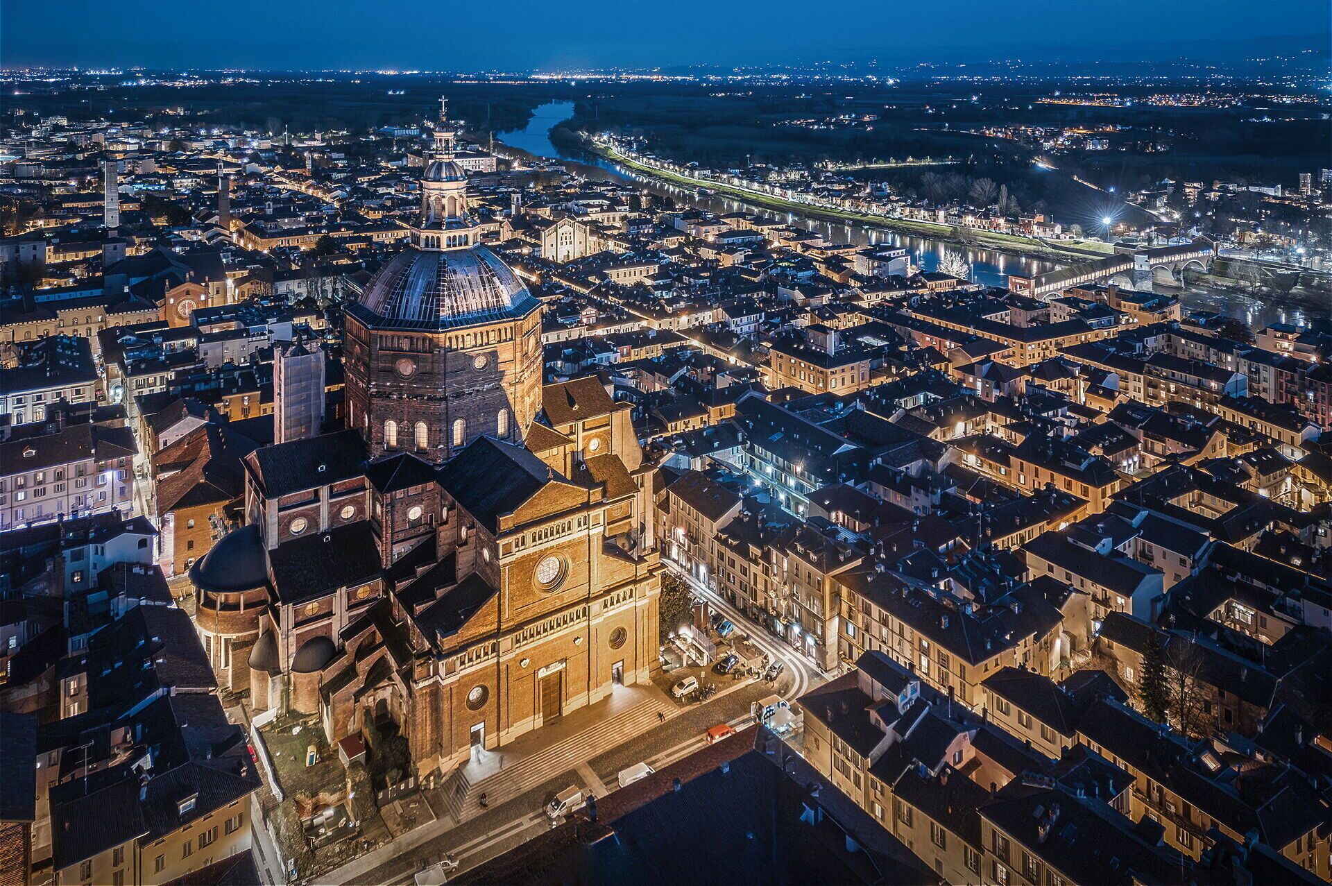 An aerial view of a cityscape at night with prominent historical architecture, including a large dome and a bell tower, and a river running through the city.