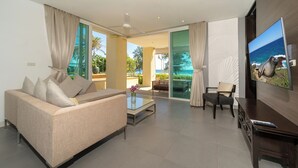 A modern living room with a sofa, coffee table, and TV, featuring a large window with a view of the ocean. - Karon Beachfront Apartment 703 (Karon)