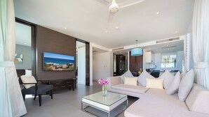 A modern living room with a sofa, a glass coffee table, and a TV displaying a scenic view. - Karon Beachfront Apartment 703 (Karon)