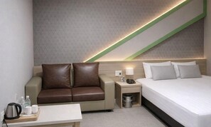 Une chambre dâhĂŽtel comprenant un lit, un canapĂ©, une table de chevet avec une lampe, une poubelle et un plateau avec une bouilloire et des tasses.