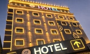 Un bĂątiment dâhĂŽtel avec une enseigne indiquant le nom de lâĂ©tablissement et la direction Ă suivre pour accĂ©der Ă lâentrĂ©e.