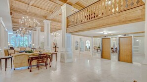 A spacious lobby with a high ceiling, chandeliers, and a wooden balcony railing. - Palm Beach Condo, Poolside Gem! Walk to Beach (Palm Beach)