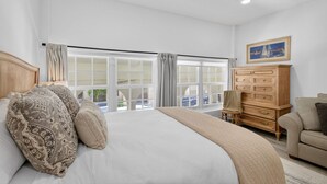 A spacious bedroom with a large bed, a wooden dresser, and a view of the outside through large windows. - Palm Beach Island Sleeps 3 Renovated Kitchen Pool (Palm Beach)