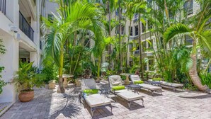 A courtyard with outdoor seating, palm trees, and a building in the background. - Palm Beach Island Sleeps 3 Renovated Kitchen Pool (Palm Beach)