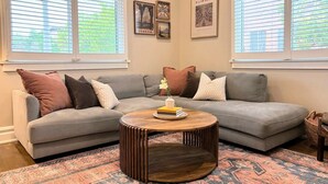 A living room with a grey sectional sofa, a round wooden coffee table, and patterned rugs. - Silver Lake Gem – 3BR Home with Backyard Oasis (Los Angeles)