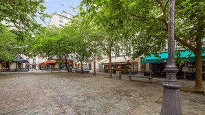 A cobblestone courtyard with trees, benches, and outdoor seating areas of cafes.
