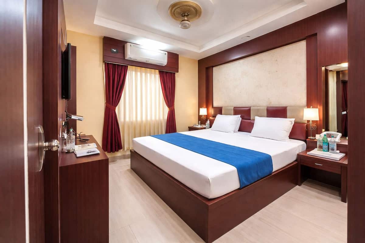 Une chambre d’hôtel comprenant un grand lit, un bureau, une chaise, une armoire, un miroir, une table de chevet, une lampe et un appareil de climatisation.