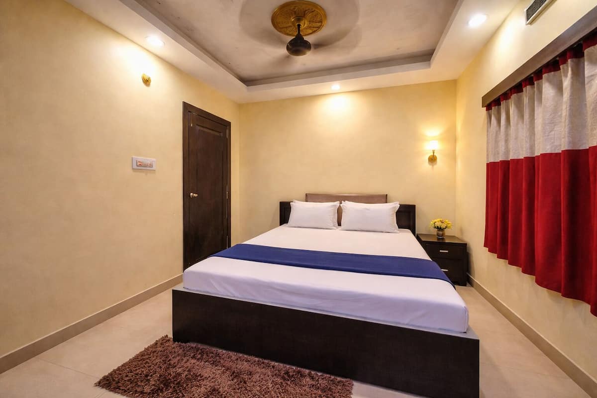Une chambre d’hôtel avec un lit, une table de chevet, un rideau rouge et un ventilateur de plafond.
