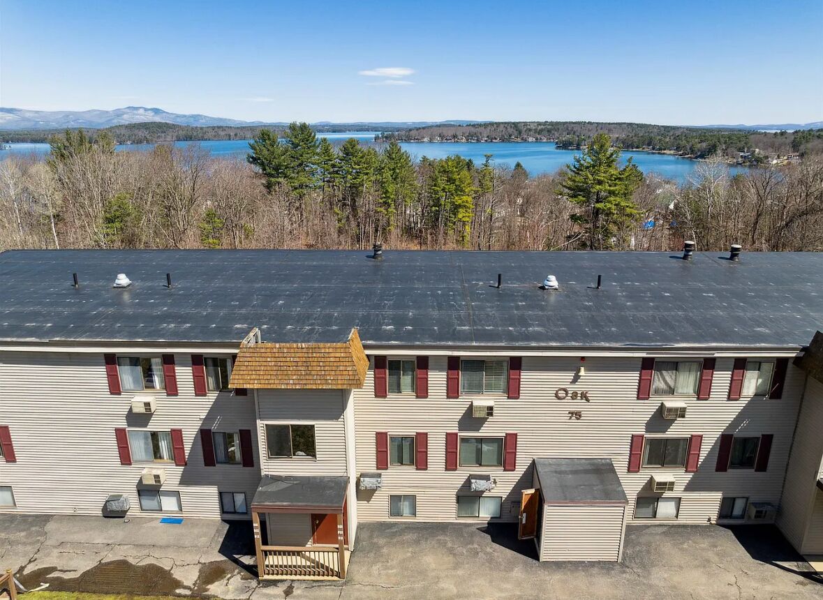 A motel with a flat roof, multiple windows, and a view of a lake and mountains.