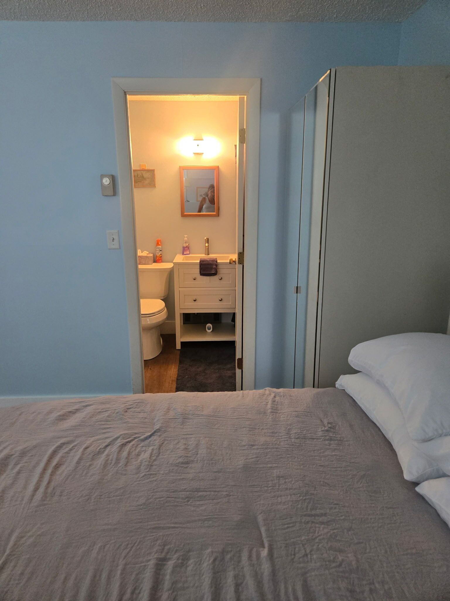 A bedroom with a bed, a door leading to a bathroom, and a visible toilet.