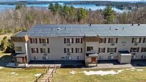 A two-story motel with a flat roof, located near a lake with a forested backdrop.