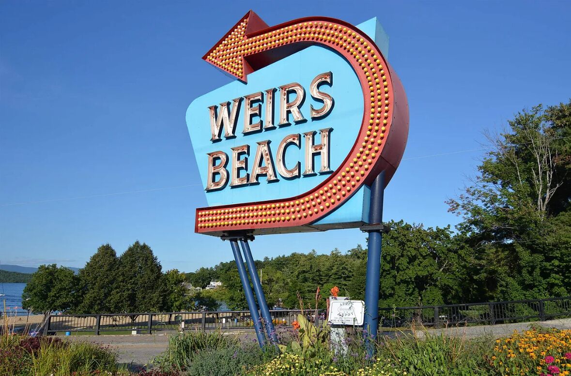 A large, curved sign with the words "Weirs Beach" in bold letters, surrounded by a decorative border.