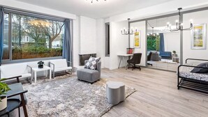 A modern living room with a fireplace, seating area, and a large window offering a view of the outdoors. - Luxury 5 Bedroom Villa w/Sauna (Vancouver)