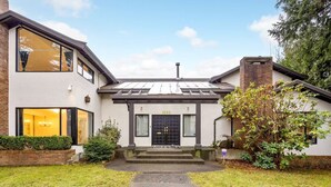 A two-story house with a black front door, a visible number '1052', and a small front yard with a pathway leading to the entrance. - Luxury 5 Bedroom Villa w/Sauna (Vancouver)