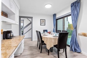 A modern kitchen with a built-in coffee maker, a dining area with a table set for four, and a view of the outdoors through a large window.