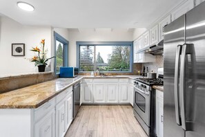 A modern kitchen with white cabinetry, a stainless steel refrigerator, and a large window providing a view of the outdoors.