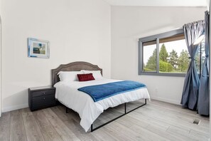 A bedroom with a bed, a nightstand, a window with curtains, and a picture on the wall.