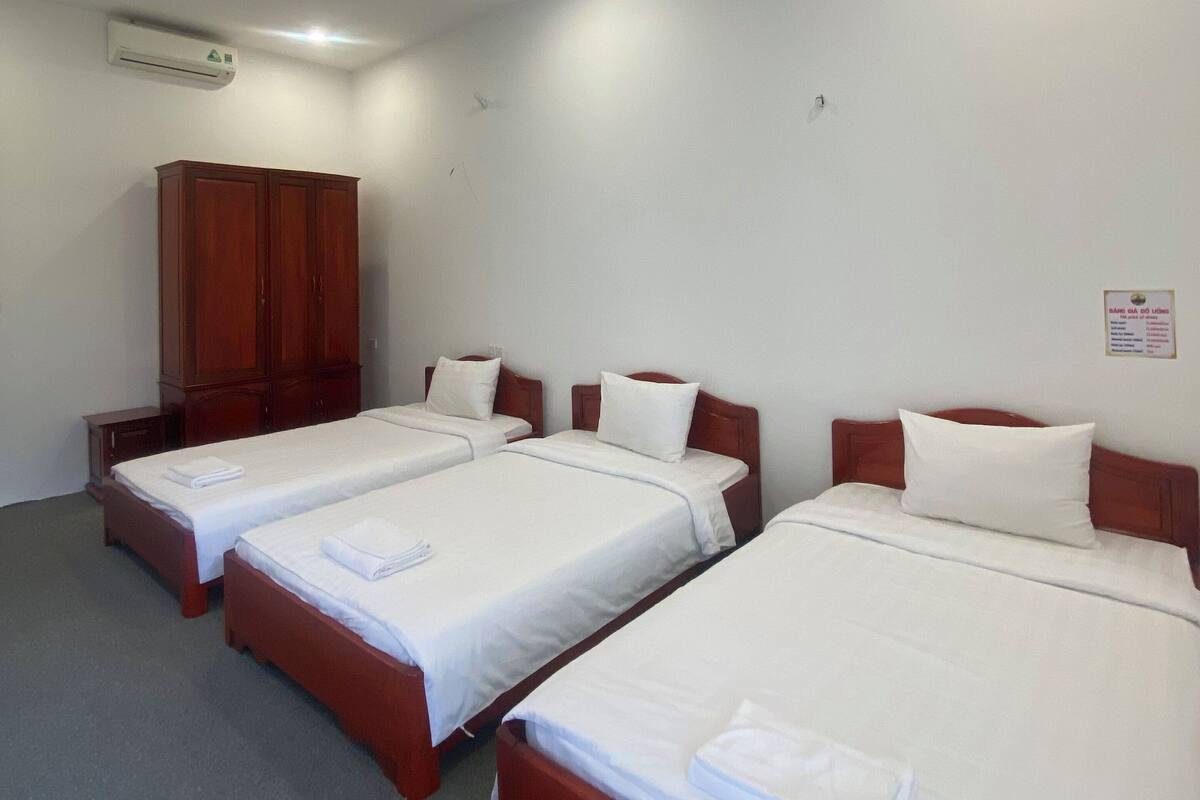 A hotel room with three single beds, a wooden wardrobe, and an air conditioning unit.