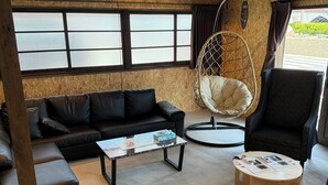 Un salon moderne avec un canapé en cuir noir, une table basse ronde en bois, un fauteuil suspendu et un fauteuil noir.