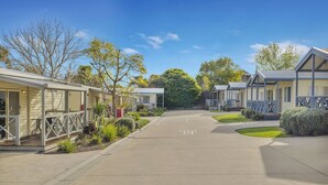 A row of single-story mobile homes with attached porches, a paved driveway, and landscaped gardens.
