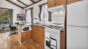 Een kleine keuken met houten kastjes, een gasfornuis, een magnetron en een koelkast.
