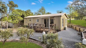 Une maison mobile d’un seul étage, de couleur beige, dotée d’un patio couvert et entourée d’une pelouse bien entretenue et de divers arbres.
