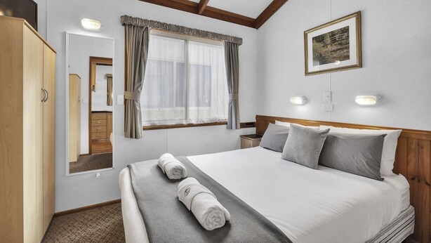 Une chambre d’hôtel avec un lit, une armoire, une fenêtre avec des rideaux, un tableau encadré au mur et des lampes de chevet.
