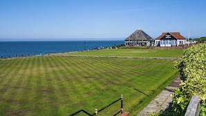 Udsigt over kysten med en græsplæne, en bygning med teksten 'Cliff Parade EBA Bowls Club' og havet i baggrunden.