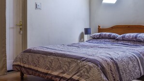 A bedroom with a bed, a door, a wall socket, and a skylight.