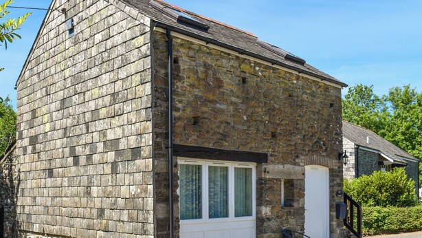 A two-story stone building with a sloped roof, a garage door, and a small porch area.