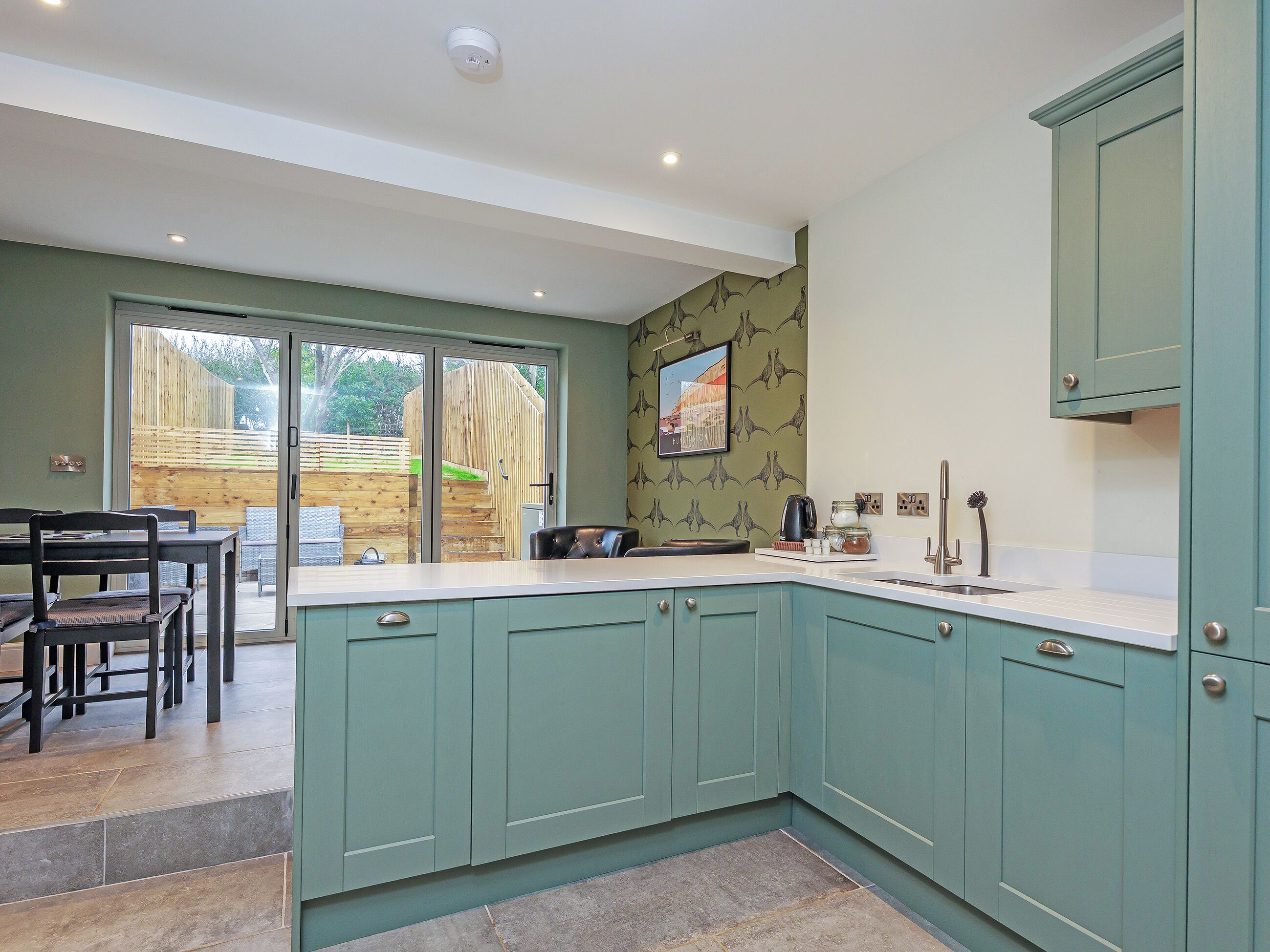 A modern kitchen with teal cabinets, a dining area with a table and chairs, and a sliding glass door leading to a patio.