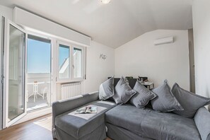 A modern living room with a grey sofa, multiple cushions, a magazine, and a sliding glass door leading to an outdoor area. - Matta Apartment 400m From The Lake (Sirmione)
