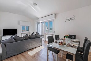 A modern living room with a grey sofa, a dining table set with plates and glasses, and a TV on a stand. - Matta Apartment 400m From The Lake (Sirmione)