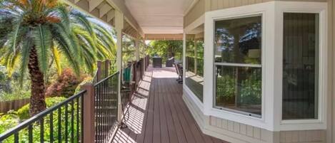 A covered outdoor area with a wooden deck, metal railing, and large windows.