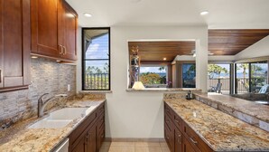 Une cuisine moderne dotée de plans de travail en granit, d’armoires en bois et d’une grande fenêtre donnant sur un balcon aménagé avec du mobilier d’extérieur.