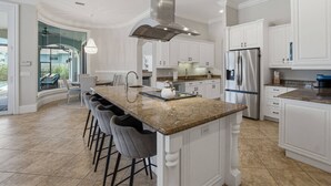 A modern kitchen with white cabinetry, a large island with bar stools, stainless steel appliances, and a view to a glass door leading outside.