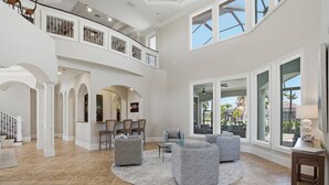 A spacious interior with a high ceiling, a dining area with chairs, a seating area with sofas, and large windows offering views.