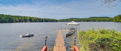 A wooden dock extending into a calm lake, with a small boat and a covered seating area at the end.