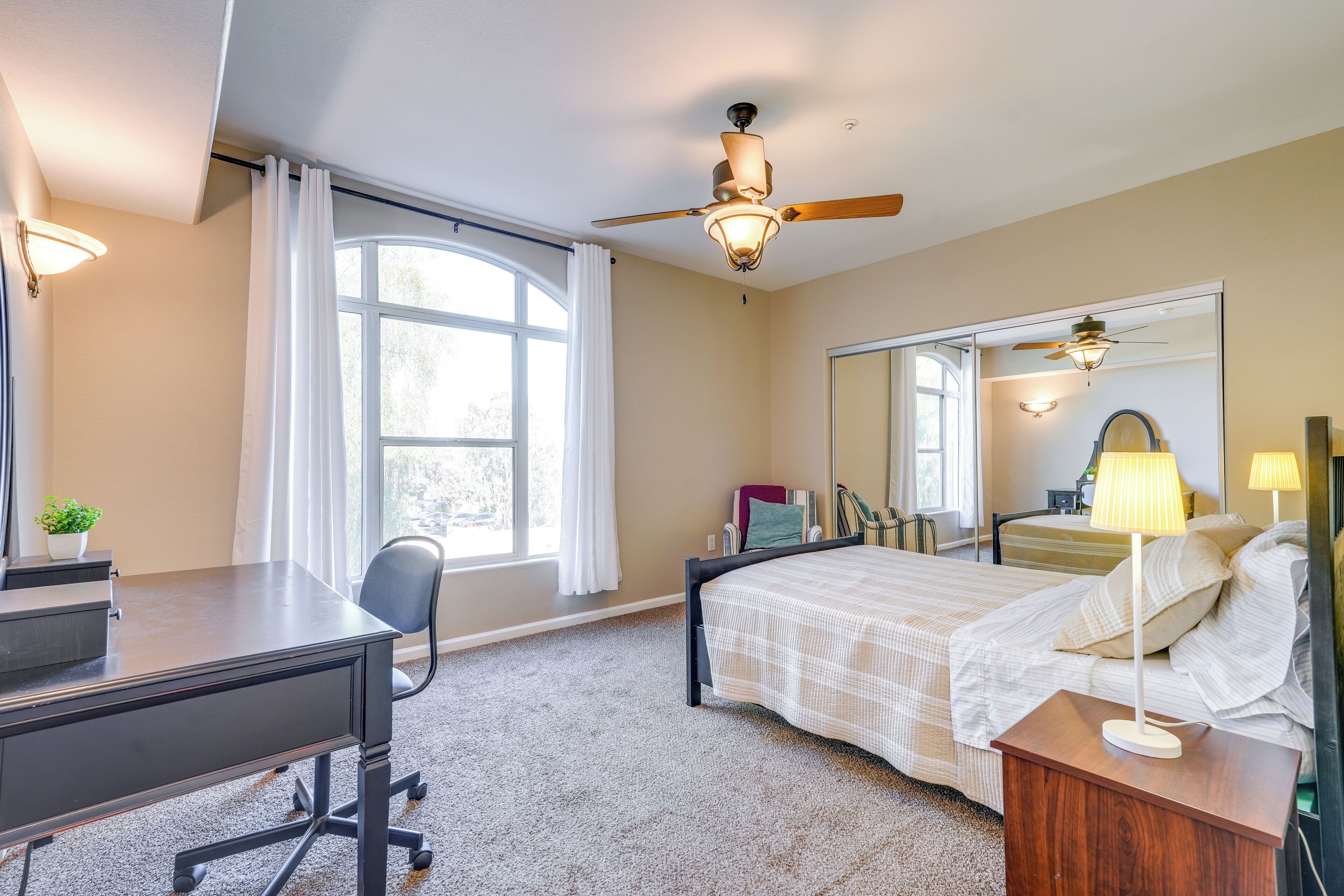 Une chambre d’hôtel avec un lit, un bureau, une chaise et une grande fenêtre.