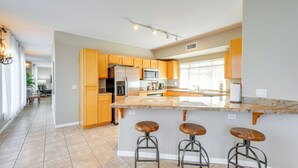 A modern kitchen with wooden cabinets, a large island with stools, and a view to the dining area. - 1 Mi to Tempe Beach Park: Well-Equipped Condo! (Tempe)