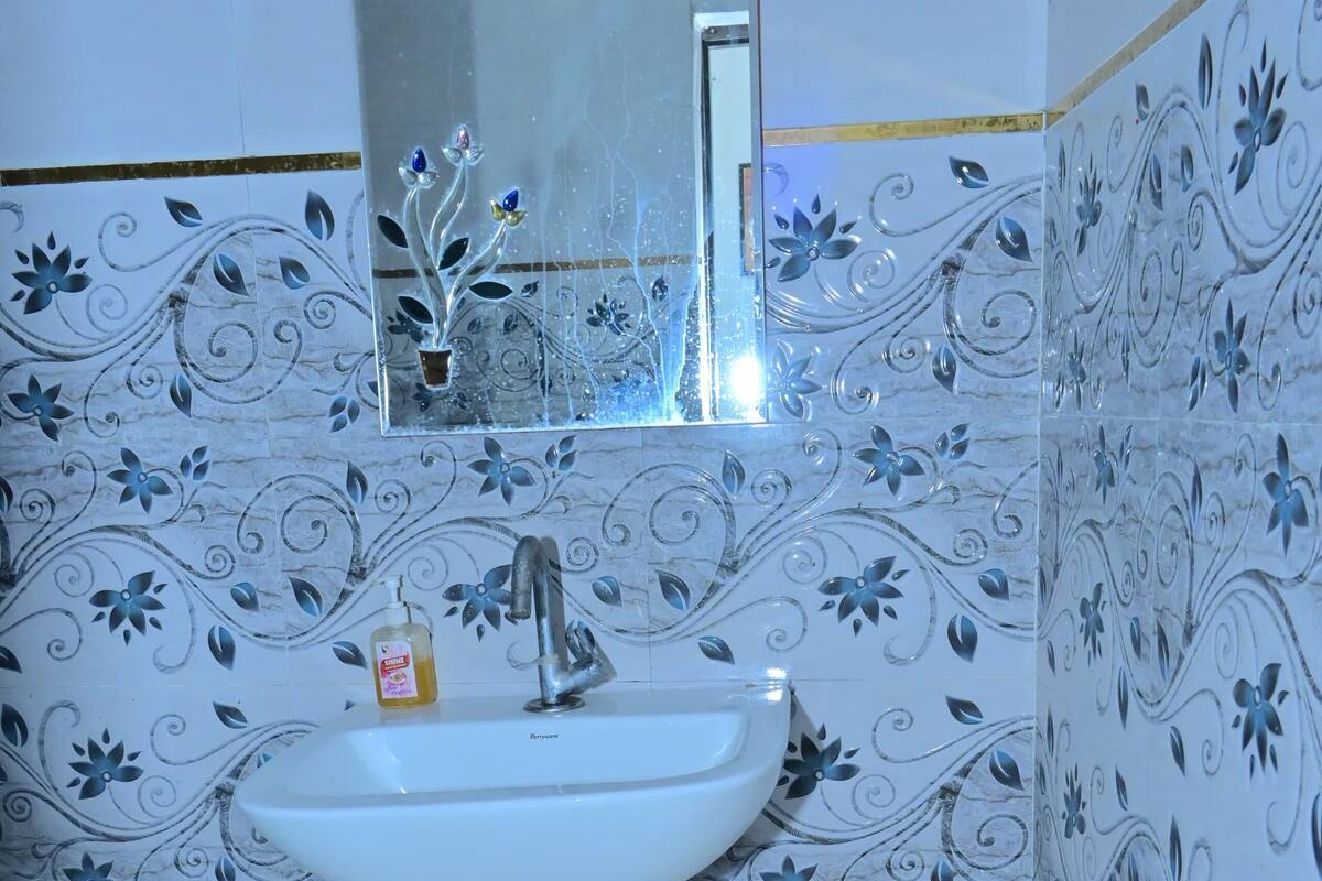 Une salle de bain avec un lavabo blanc, un miroir et des carreaux décoratifs bleus et blancs à motifs floraux.