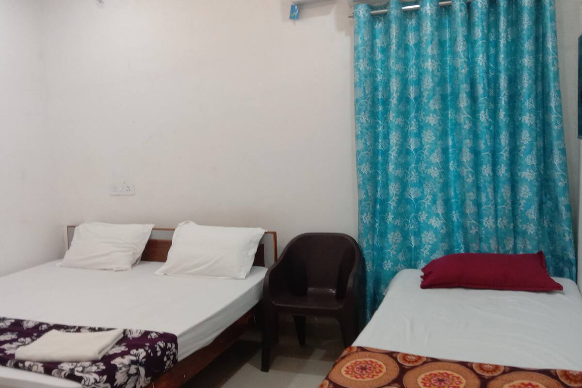 Une chambre avec deux lits, une chaise et un rideau.