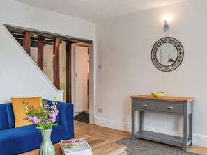 En stue med en blå sofa, et træbord, en vase med blomster, et magasin, et gråt konsolbord med en gul skål, og et spejl på væggen.
