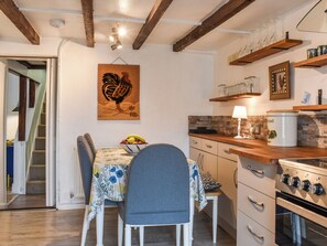 A kitchen with wooden beams, a dining table with chairs, a fruit bowl, and a stove.