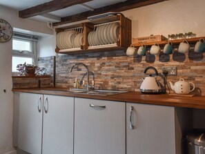 Una cocina con encimera de madera, un fregadero, una tetera y una estantería con frascos y tazas.