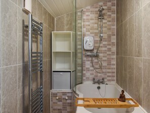 Un baño con bañera, ducha e inodoro. Hay un mueble con un pequeño armario y una repisa.