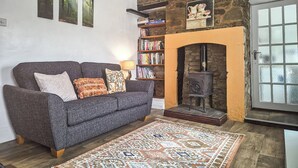 Una sala de estar acogedora con un sofá gris, cojines estampados, un tapete con diseño, una estantería y una chimenea de piedra.