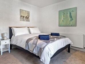 A bedroom with a bed, a nightstand, a lamp, and two paintings on the wall.